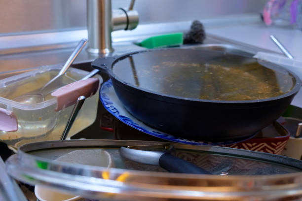 Selective focus on a frying pan in a pile of dirty dishes in the kitchen sink.