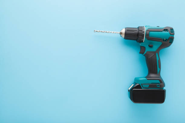 istock Dark black green professional battery driver drill on light blue table background. Pastel color. Closeup. Tool for repair work. Top down view. Empty place for text. 1478060589
