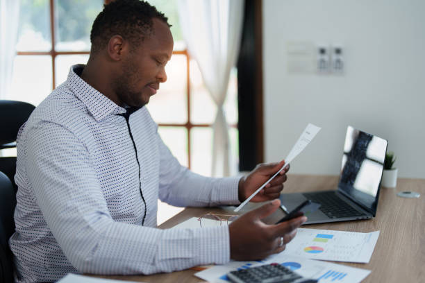 istock middle aged man American African using smart phone mobile and laptop computer with planning working on financial document, tax, exchange, accounting and Financial advisor 1478062387