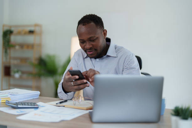 istock middle aged man American African using smart phone mobile and laptop computer with planning working on financial document, tax, exchange, accounting and Financial advisor 1478062438