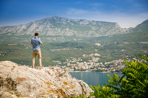 The tourist man looking at the town Herceg Novi in the Bay of Kotor in Montenegro, standing on the edge of the cliff
