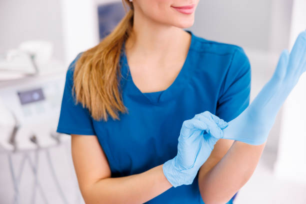 Female doctor putting on protective latex gloves Female doctor putting on protective surgical gloves while working in hospital; dentist putting on medical latex gloves before oral surgery procedure putting on latex gloves stock pictures, royalty-free photos & images