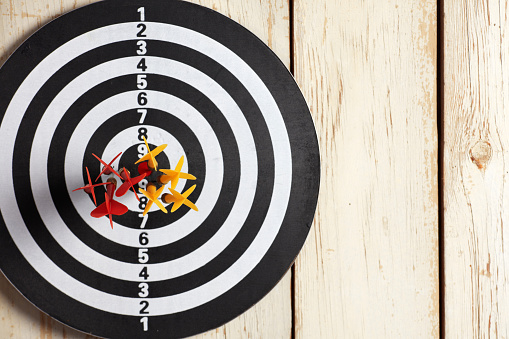 Dartboard hanging on a wooden wall and red yellow darts are grouped at the center