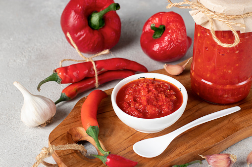 Traditional sauce adjika with hot chili pepper, paste harissa in white bowl on wooden board