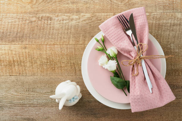 istock Easter brunch table setting. Spring Easter holiday concept with white, pink plate and napkin with decorative symbols holiday rabbit, eggs and bouquet of flowers on old wooden background. Top view. 1478086620