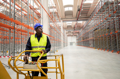 Afro-American logistic worker during his job on industrial lifter in warehouse