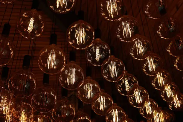 Photo of Stylish, modern and decorative lamps of Edison of round shape in the rows. Light bulbs in retro style. A lot celling glowing vintage LED lamps. Object for interior decoration, selective focus photo