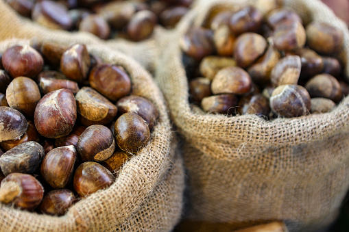 high angle view of some chestnuts out from a paper cone, on a rustic wicker mat, on a table next to some autumn leaves