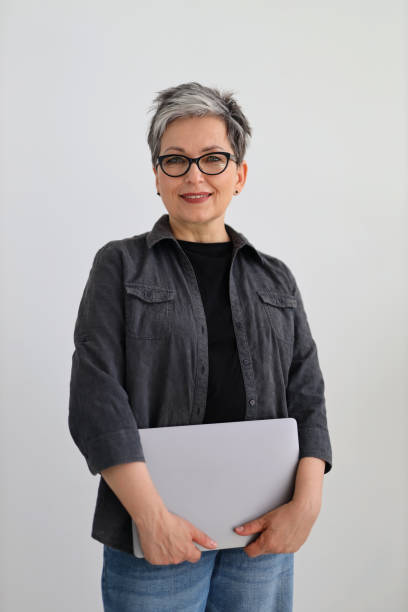 istock Senior woman with a laptop in her hands, glasses on a gray background, a programmer. 1478105721