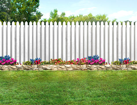 Empty backyard with green grass, flowers and a white picket fence
