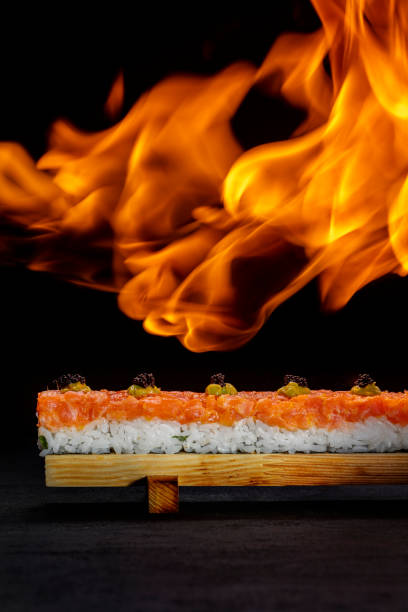 Oshi sushi with salmon, rice, microgreens and wasabi stuffed with shrimp meat. Oshi sushi stands on a special, wooden, light stand. The stand stands on a black paper background. A fire burns over oshi sushi. sushi oshi con salmón, arroz, microgreens y wasabi relleno de carne de camarones. el sushi oshi se encuentra en un soporte especial, de madera y ligero. el soporte se encuentra sobre un fondo de papel negro. un incendio arde sobre el sushi oshi.