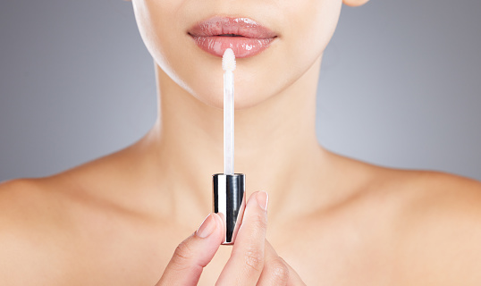 Woman, lips and lip gloss application for beauty, makeup shine and skincare wellness in grey background studio. Model, lipstick tool or brush for cosmetics dermatology glow or luxury salon product