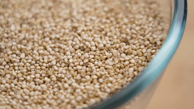 Uncooked quinoa grains falling into a glass bowl