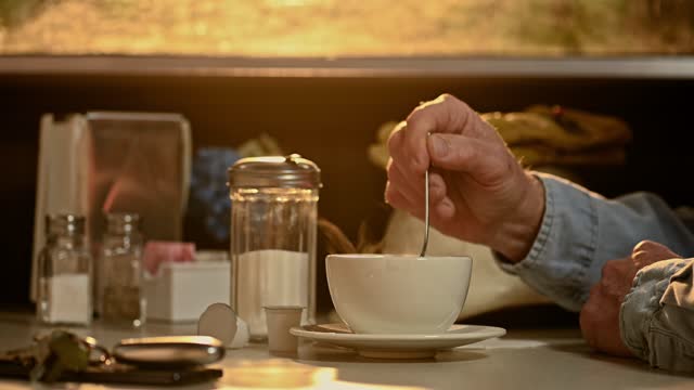A construction worker adding sugar to his steaming hot cup of coffee in a diner at sunrise