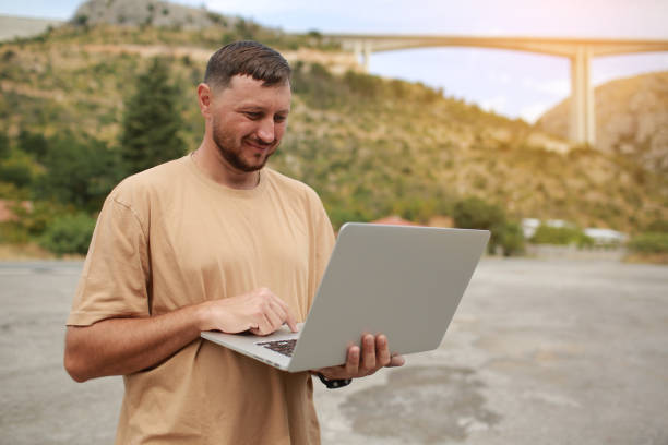 istock Collected man in casual clothes working on laptop outdoors on bridge construction background. Concept of remote work engineer or freelancer lifestyle. Cellular network broadband coverage. internet 5G 1478112629