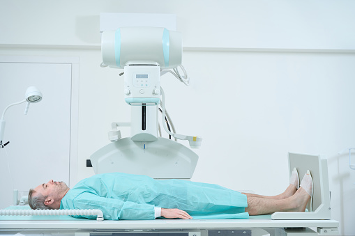 Adult man lying on a bed and waiting for X-Ray machine to scan in hospital. Modern hospital with technologically advanced equipment