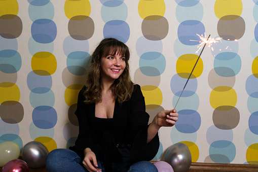 Young Woman Sitting with a Sparkler Against Colorful Background