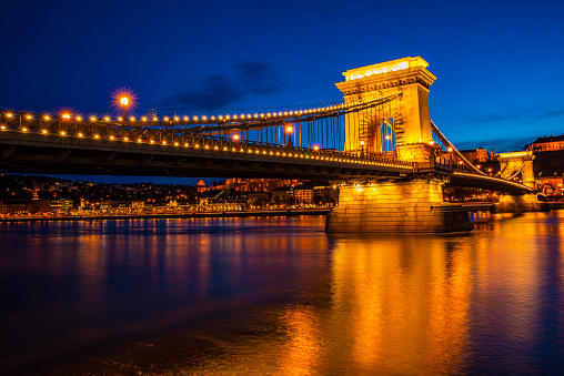 Ancient Chain bridge on Danube river in Budapest city with lanterns for nighttime backlighting and blue sky.