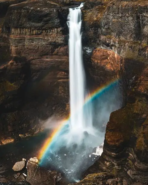 A landscape of Haifoss waterfall with a vivid rainbow arching above it, cascading over the rocky terrain below