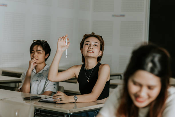 Asian architecture student asking question to teacher while attending lecture class, school of architecture and design Happy hipster Thai university student raised hand up and asking some question about content that professor is teaching in class. nonbinary teacher stock pictures, royalty-free photos & images