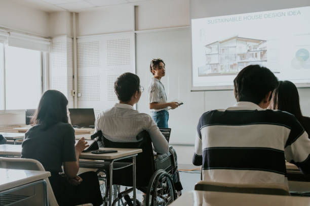 Disability architect student sitting on his wheelchair and listening classmate presents her work in front of the class. Asian disability architect student sitting on his wheelchair, equality to everyone to access the best education now, school of architecture and design lecture class interior designing course stock pictures, royalty-free photos & images