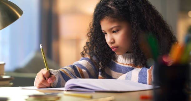 istock Child, learning and writing in notebook for education or studying for school exam or test at desk. Girl kid student with pencil for notes in book with focus on development, knowledge or study at home 1478130100