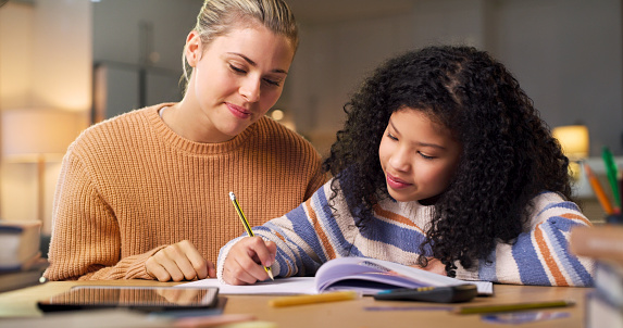 Woman teaching, child writing and learning for home assessment, test and memory development at night. Personal tutor, mother or family support, helping and creative biracial kid or student education