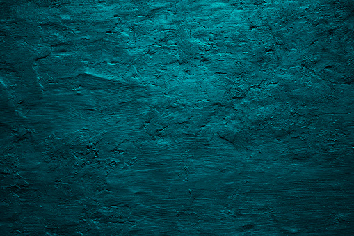 Dark green blue uneven texture. Painted old wall with plaster. Petrol color. Grunge surface background for design. Light and shadow. Rough grainy. Empty. Close-up.