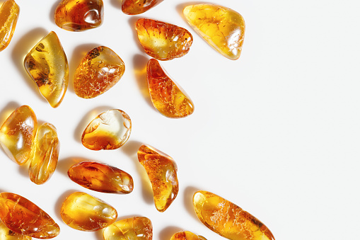 Amber stones on white background, transparent stone yellow beige gradient color. Natural gemstone mineral material, healing crystal. Top view Amber textured fon. Nature gems, frame with copy space.