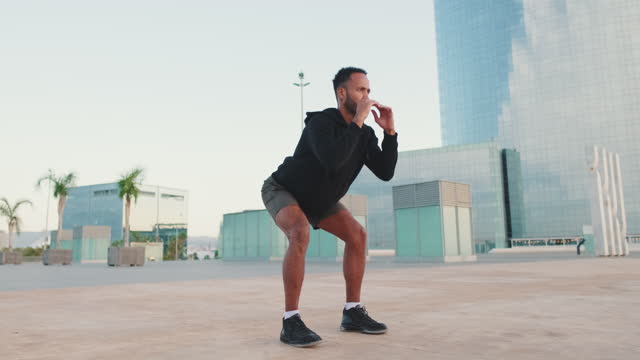 Young bearded male athlete doing workout, squats on the waterfront