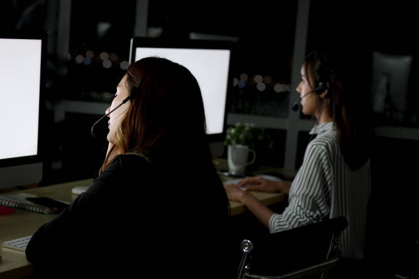 istock Back side of night shift staff group with headphone work at call center customer service desk at night, looking at desktop computer, typing answer question, worker hands-free phone work hard overtime. 1478149297