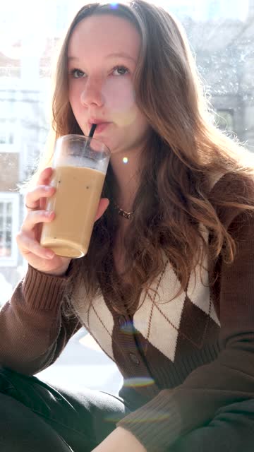 Close-up of happy woman drinking smoothie with straw, looking at camera, in slow motion