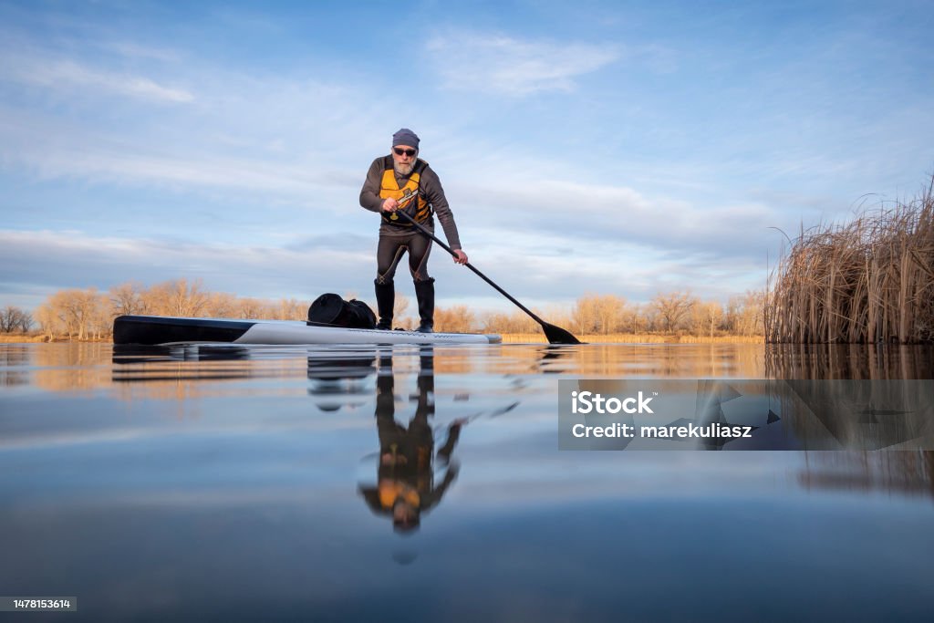 senior paddler on his paddleboard on lake in winter or early spring in Colorado senior paddler on his paddleboard on lake in winter or early spring in Colorado, frog perspective (partially submerged action camera) Senior Adult Stock Photo