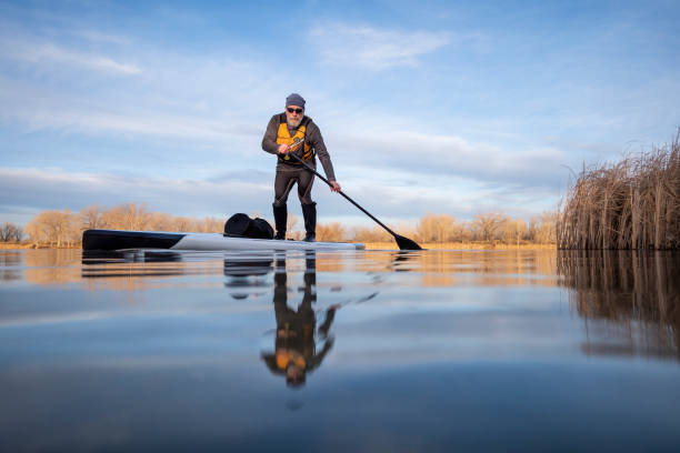 senior paddler on his paddleboard on lake in winter or early spring in Colorado senior paddler on his paddleboard on lake in winter or early spring in Colorado, frog perspective (partially submerged action camera) paddleboard surfing water sport low angle view stock pictures, royalty-free photos & images