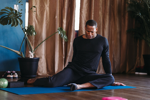 A black man does a seated stretch for hip mobility while attending a group fitness class at a boutique fitness studio.