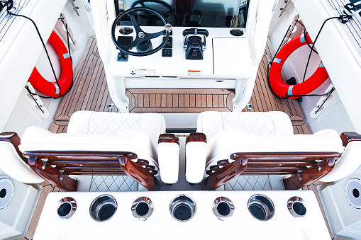 Luxurious boat control cabin with white leather seats, steering wheel, gear lever and on-board computer.