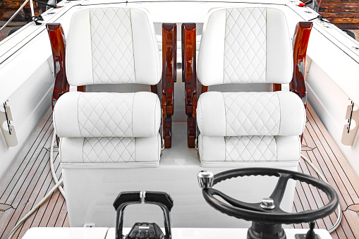 Luxury motorboat control cabin with white leather seats, steering wheel and gear lever.