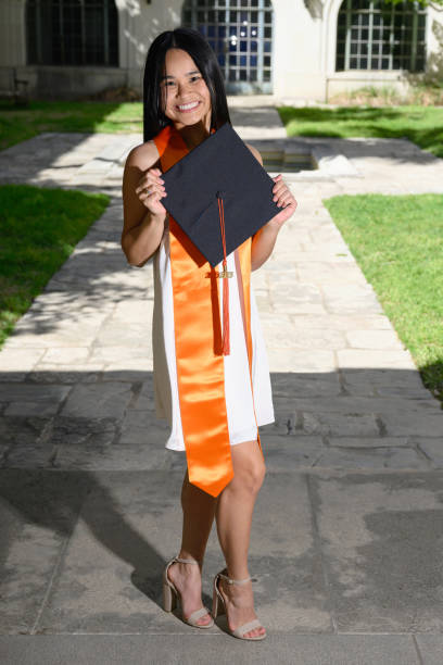 Young attractive Asian American girl with cap and gown preparing for college graduation