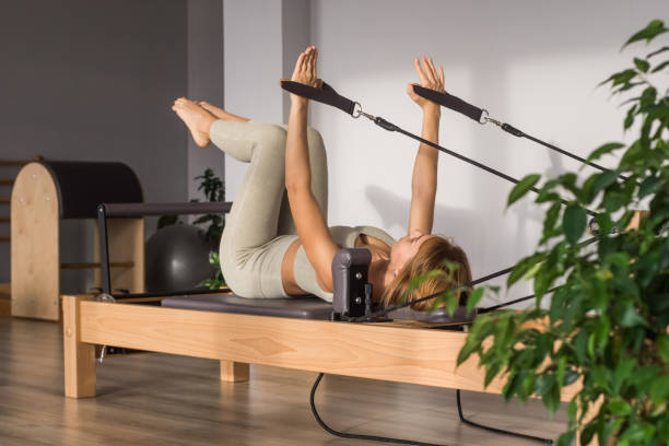 Woman training pilates on the reformer bed. Reformer pilates studio machine for fitness workouts in gym. Fit, healthy and strong authentical body. Fitness concept stock photo