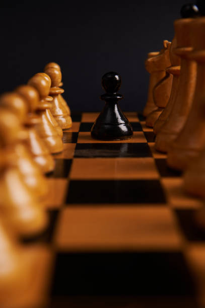 istock Selective focus on a black pawn between white chess pieces on the chessboard, isolated on black background. 1478160474