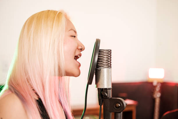 Female Korean Musician practising at home recording studio. She is dressed in casual black dress .  Interior of home recording studio.
