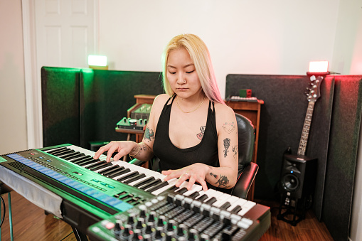 Female Korean Musician singing and playing keys at home recording studio. She is dressed in casual black dress .  Interior of home recording studio.