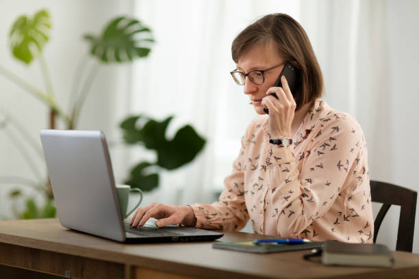 istock Woman in pajamas using laptop computer and smart phone in home office 1478163294