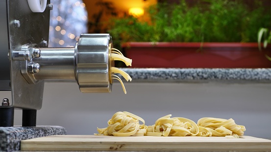 Making Traditional raw Italian homemade pasta with egg. Spaghetti comes out of pasta machine.