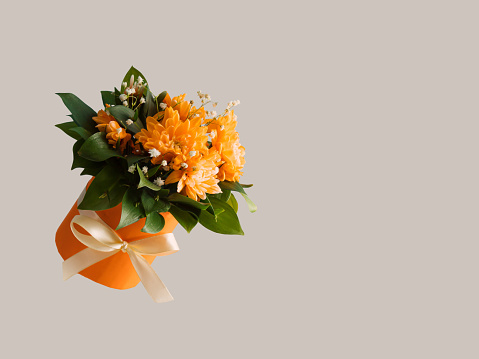 Orange gift box with spring flowers and leaves on grey background. 8 March or Mother's Day card idea. Copy space.