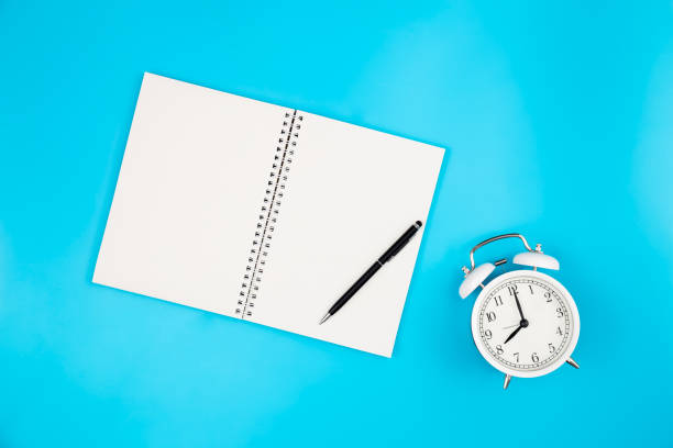 istock White blank notepad and alarm clock on blue background, flat lay. 1478182973