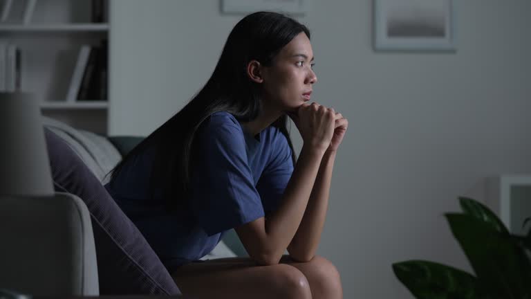 Young Asian woman sitting on sofa at home feeling sad tired and worried suffering depression in mental health.