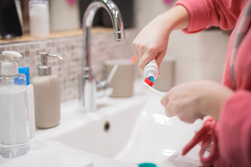 Female hands handling toothpaste and a tooth brush in a bathroom, close-up