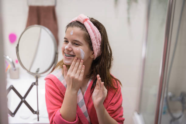 Happy teenage girl applying moisturizing face cream stock photo
