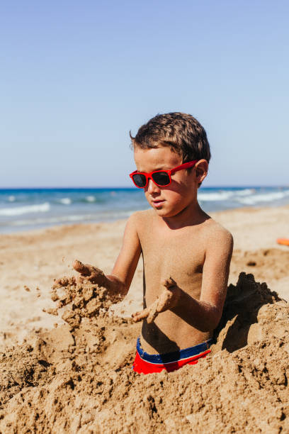 istock Playful boy digging in to the sand on the beach 1478189942